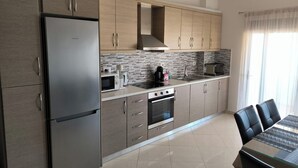 Una cocina moderna con un refrigerador de acero inoxidable, armarios de madera, salpicadero de azulejos y un comedor con mesa de vidrio y sillas negras.