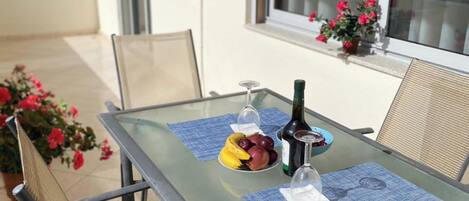 A glass-top table with a bottle of wine, a bowl of fruit, and a wine glass on a blue placemat.