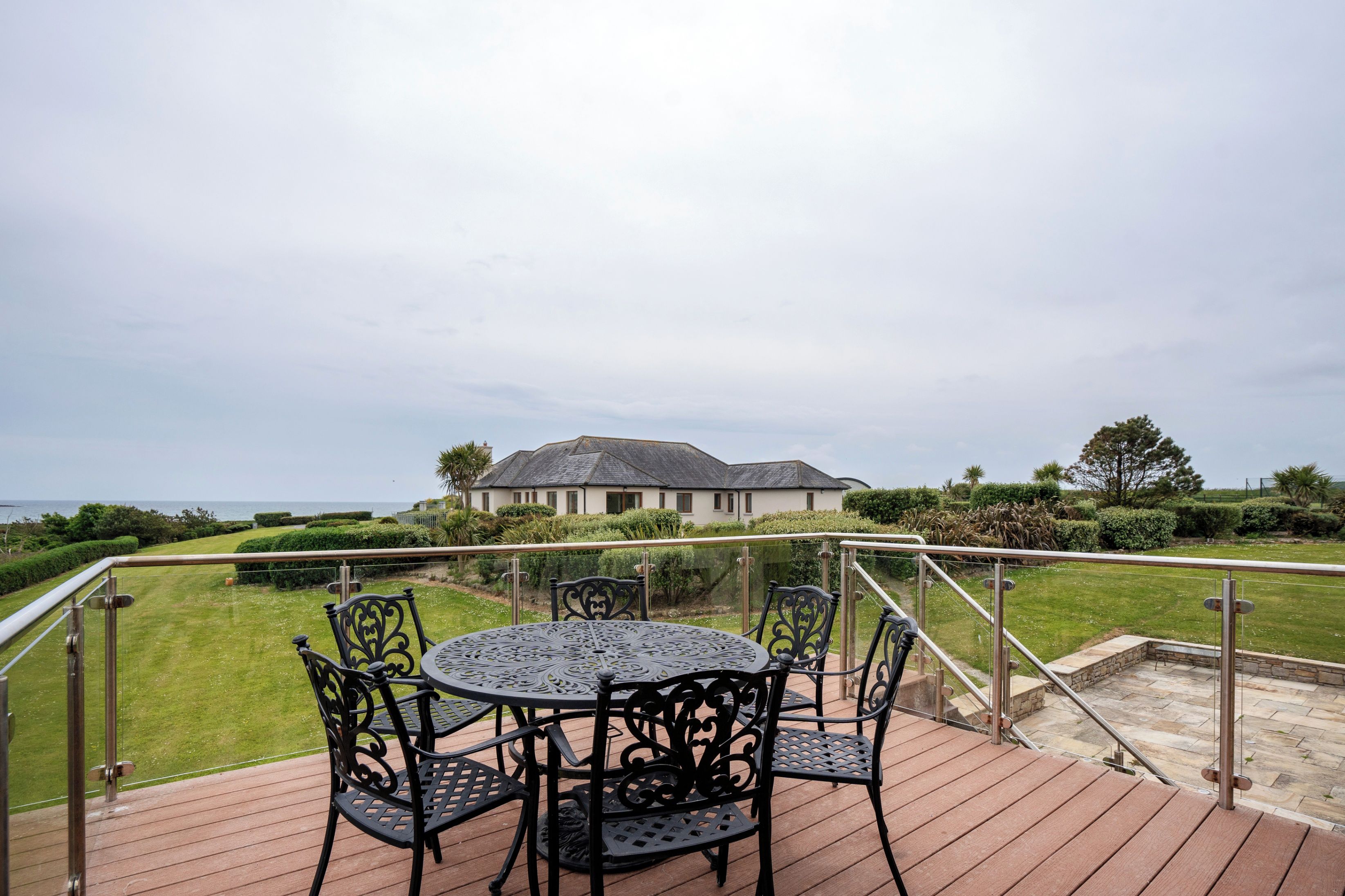 A deck with a round table and chairs, overlooking a lawn and a building with a sloped roof.
