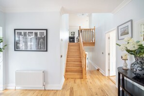 A hallway with a wooden staircase, a radiator, and framed artwork on the walls.