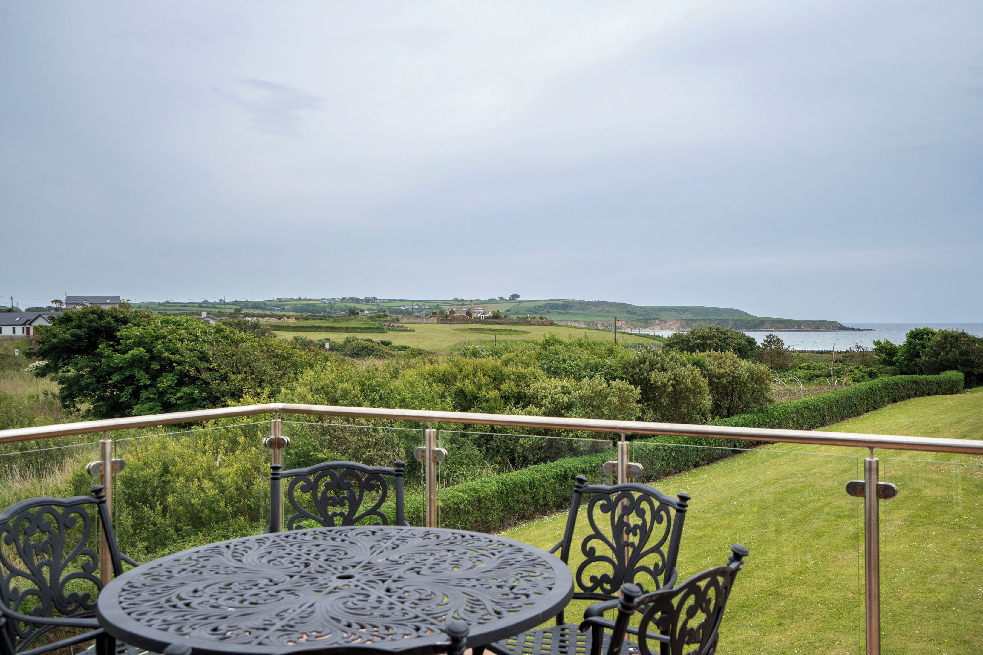 A terrace with a round table and chairs, overlooking a coastal landscape with hills and a body of water.