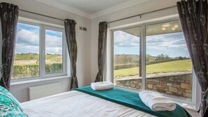 Ein Schlafzimmer mit Bett, Blick auf die Landschaft und Vorhängen.