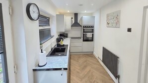 A narrow kitchen with a built-in oven, a sink, and a clock on the wall.