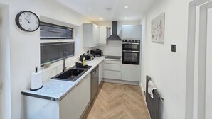 A compact kitchen with a sink, stove, and oven, a clock on the wall, and a radiator on the floor.