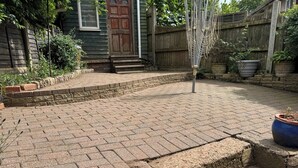 A paved patio with brick flooring, a wooden door, and a blue planter.