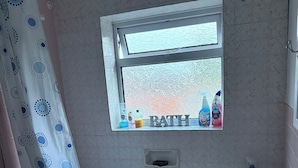 Une salle de bain avec une baignoire, une fenêtre avec des articles de toilette, un rideau de douche et un porte-serviettes.