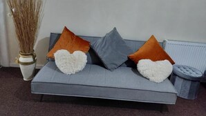 Un canapé gris avec trois coussins, un vase contenant des plantes séchées et un radiateur.