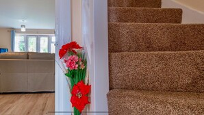 A living room with a beige sofa, a flat-screen TV, and a staircase with brown carpeted steps. - Cosy Home-Sleeps 5- Private Garden- Free Parking (Corby)