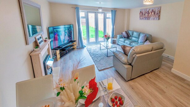 A living room with a television, sofa, coffee table, and dining area with a table set for two. - Cosy Home-Sleeps 5- Private Garden- Free Parking (Corby)