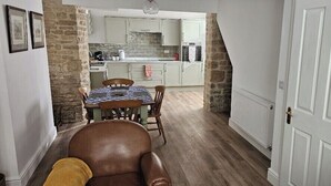 A dining area with a table and chairs, a kitchen in the background, and a white door. - Stylish 2-Bed House in Stamford Town Centre (Stamford)