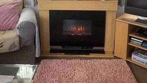 A living room with a fireplace, a framed picture above it, a sofa, a TV, and a pink rug. - 2Bed Caravan Sleeps 6- Beach Access, Pets, Parking (Mablethorpe)
