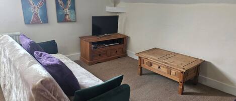 A room with a sofa, a wooden coffee table, a TV stand, and two wall-mounted paintings.