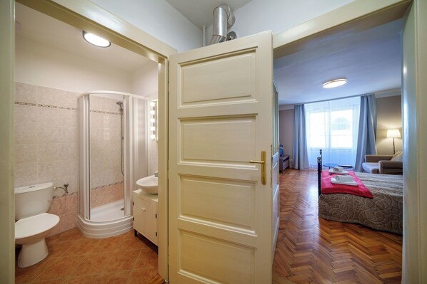 A hotel room with a shower, toilet, and a bed with a red blanket.