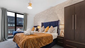 Ein Hotelzimmer mit einem großen Bett, einem Kleiderschrank, einem Fenster mit Vorhängen und Blick auf umliegende Gebäude.
