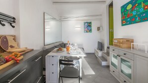 A modern kitchen with a dining table, chairs, and a bench. There is a fruit bowl, a bottle, and a glass on the table. The kitchen has white cabinets and a wooden countertop. - Un Terrazzo Nella Pigna, Sea-View Terrace, Sanremo, Italy (Sanremo)