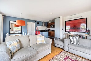 A living room with two grey sofas, a red pendant light, and a large abstract painting on the wall. - 2br-sleeps4-pool-freeparking-trenythonestate (Par)