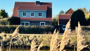 Een huis met een rood pannendak, een vijver op de voorgrond en een haag op de achtergrond.