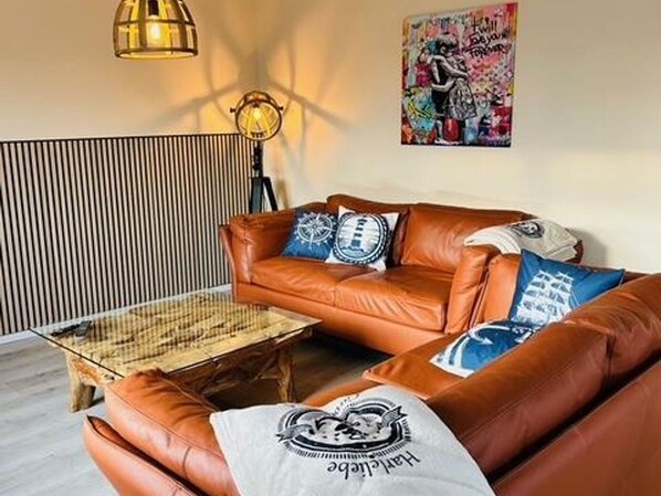 Un canapé en cuir marron agrémenté de coussins à motifs, une table basse en verre et une lampe fixée au mur.