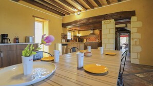 A dining area with a wooden table set for four, surrounded by chairs, with a view of the kitchen in the background. - Villa Haut Briauche (61) - Heated pool - Beach Volley - 2h Paris - 45p (Eperrais)