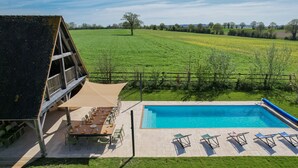 A poolside area with a wooden deck, outdoor seating, and a view of a green field. - Villa Haut Briauche (61) - Heated pool - Beach Volley - 2h Paris - 45p (Eperrais)