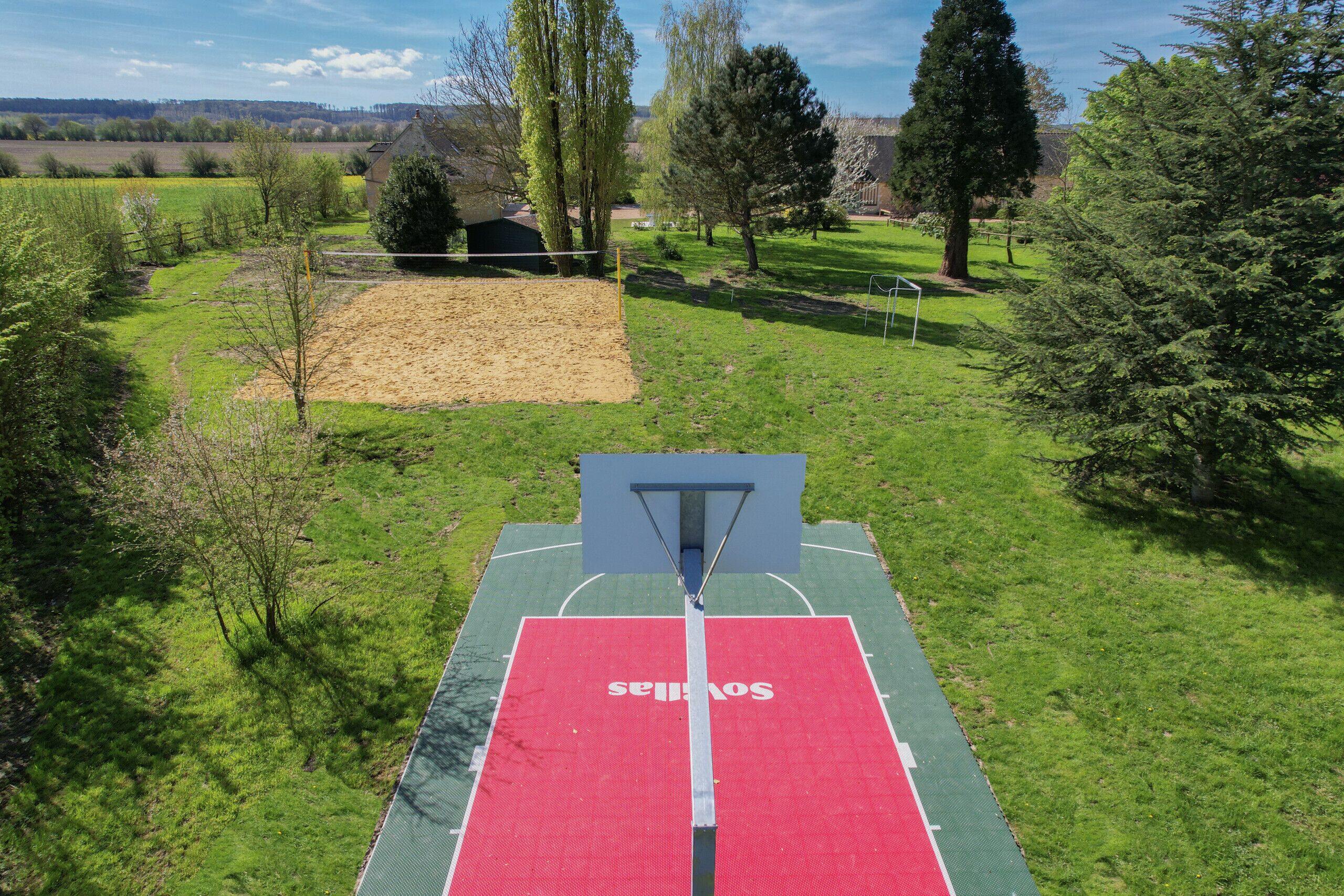 A basketball court with a net, surrounded by trees and open fields.