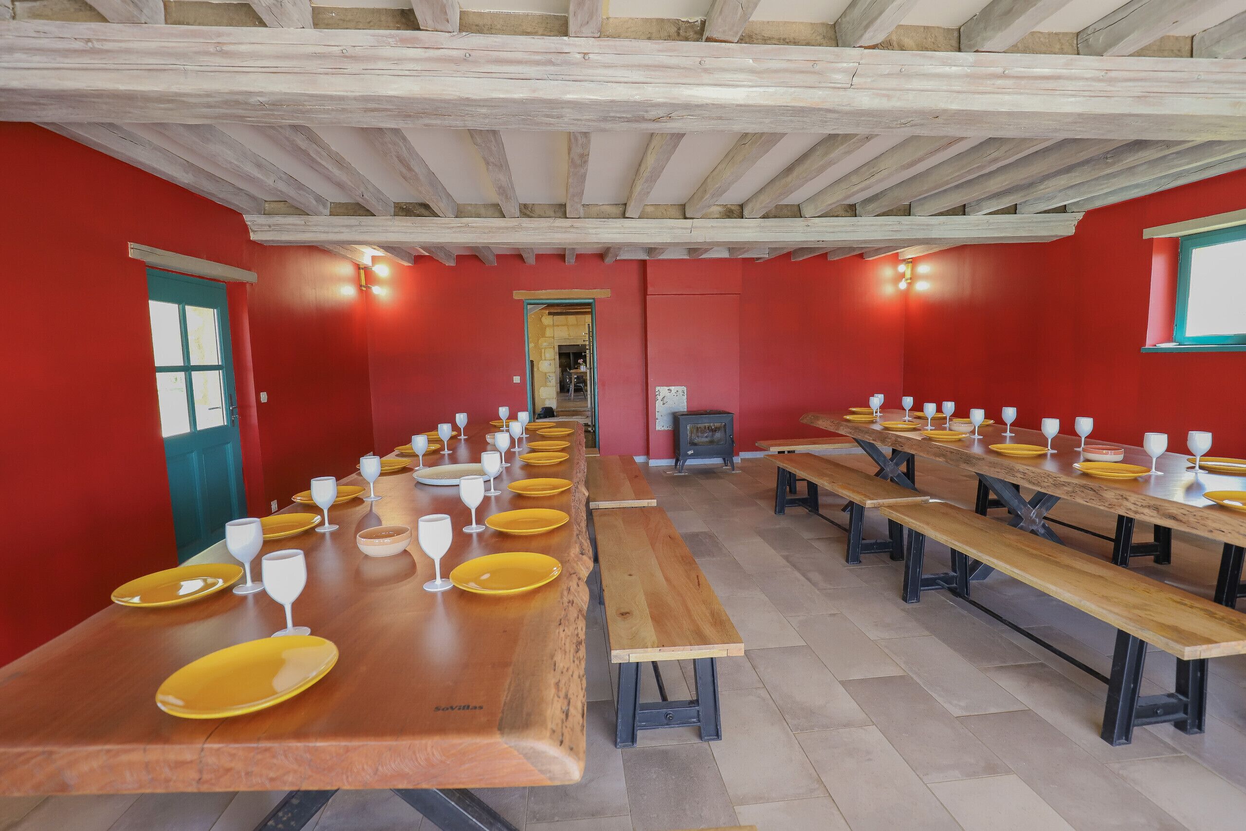 A long dining table with benches, red walls, and wooden beams on the ceiling.