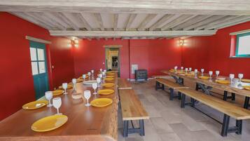 A long dining table with benches, red walls, and wooden beams on the ceiling.