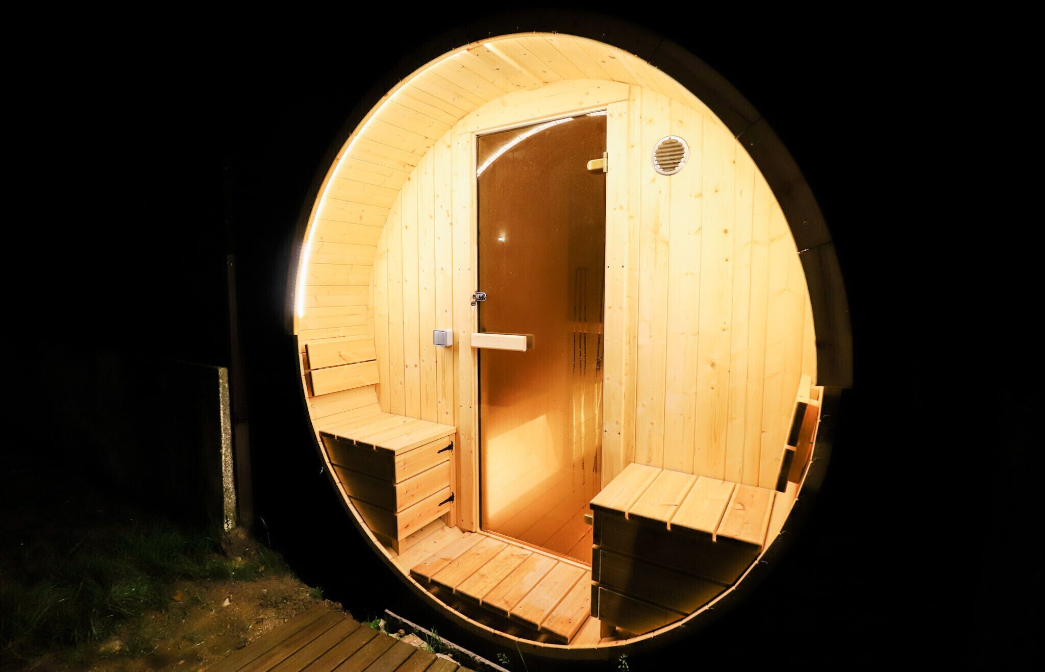 Un sauna circulaire en bois, doté d’une porte, de bancs et d’une petite fenêtre.