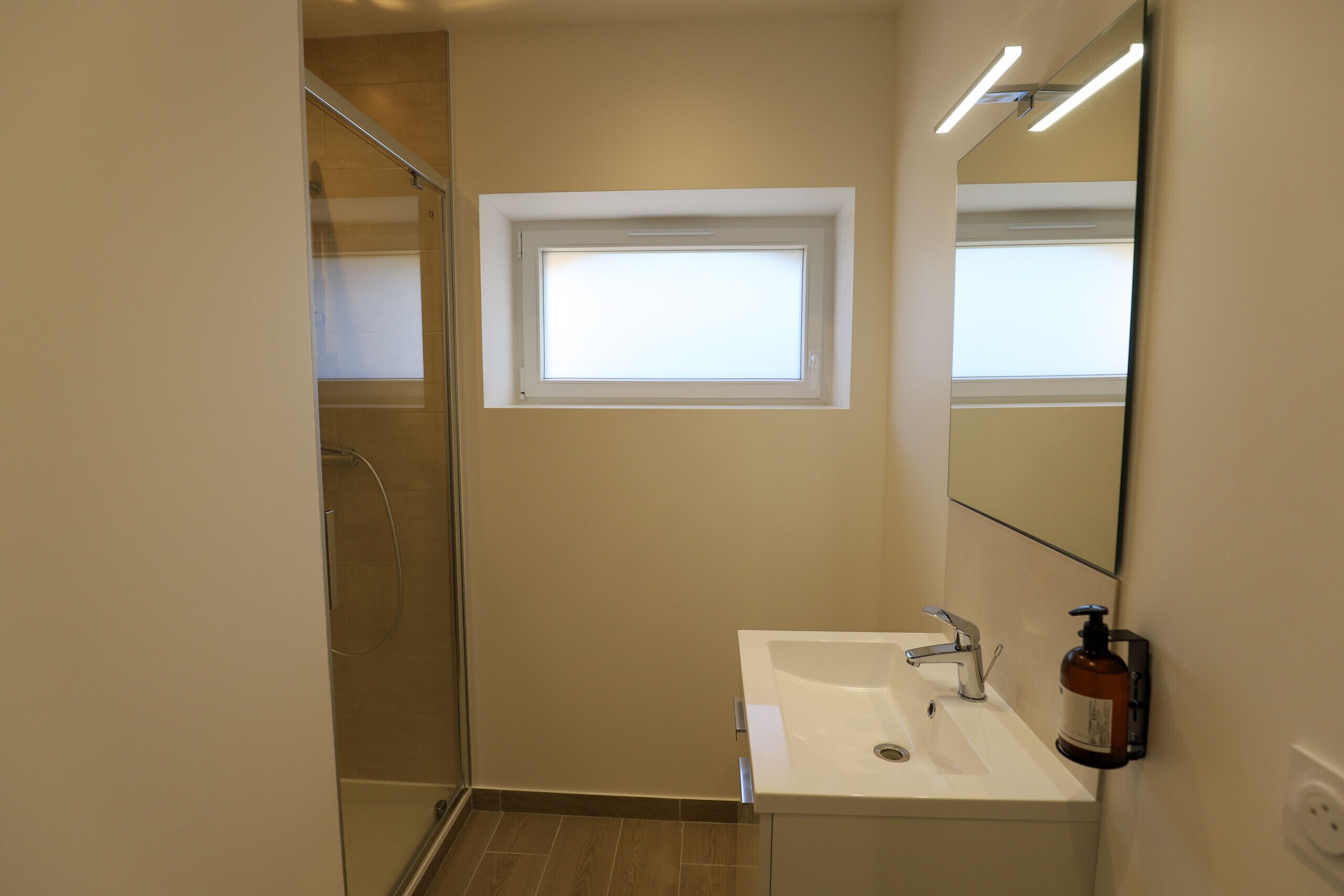 Ein Badezimmer mit Dusche, Waschbecken, Spiegel und Fenster.