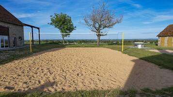 Ein Sandvolleyballfeld mit Netz, umgeben von Gras und Bäumen, mit Gebäuden im Hintergrund.