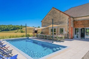 A pool with lounge chairs, a barbecue area, and a dining table with chairs.