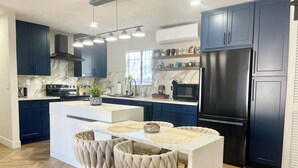Une cuisine moderne avec des meubles de couleur bleu foncé, un réfrigérateur en acier inoxydable et un îlot central blanc doté de deux chaises rembourrées.