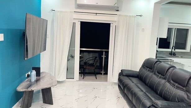 A modern living room with a black leather sofa, a small table with a vase, and a TV mounted on a blue wall.