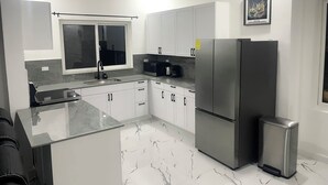 A modern kitchen with white cabinets, a stainless steel refrigerator, and a marble floor.