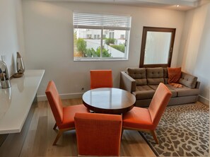 A modern living room with a round table and orange chairs, a grey sofa with a patterned throw, and a view of a building through a window with blinds. - Charming 4-bedroom Townhouse in pleasant Los Angeles FREE AC, WiFi and Parking (Los Angeles)