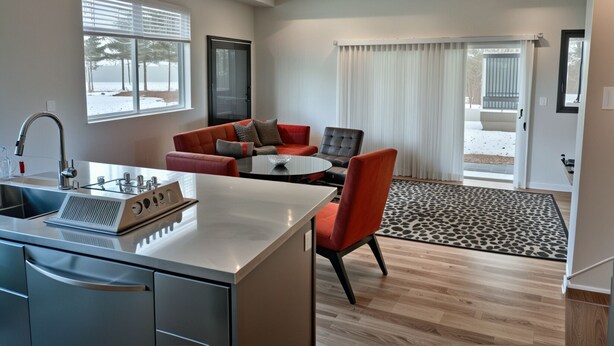Una cocina moderna con estufa integrada, un comedor con sofá rojo y una mesa redonda, y vista al exterior a través de un ventanal.