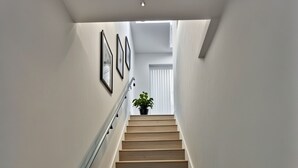 Una escalera con escalones de madera y barandilla de metal, que conduce a una habitación con una planta en maceta y cuadros en la pared.