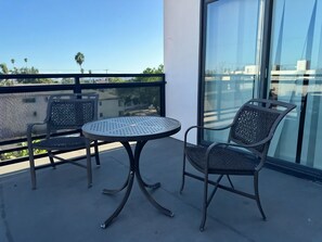 A balcony with two chairs and a round table, overlooking a cityscape with palm trees. - Charming 4-bedroom Townhouse in pleasant Los Angeles FREE AC, WiFi and Parking (Los Angeles)