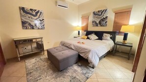 Une chambre à coucher comprenant un lit, une table de chevet, une lampe, un banc et deux climatiseurs fixés au mur.