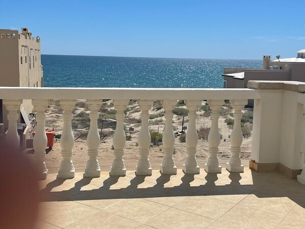 Un balcone con ringhiera bianca che si affaccia su una spiaggia sotto un cielo azzurro terso.