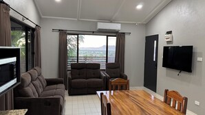 A modern living room with a sofa, armchair, dining table, and TV. - Dovu Residences (Labasa)