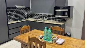 A compact kitchen with dark cabinets, a microwave, a sink, and a dining table with chairs. - Dovu Residences (Labasa)