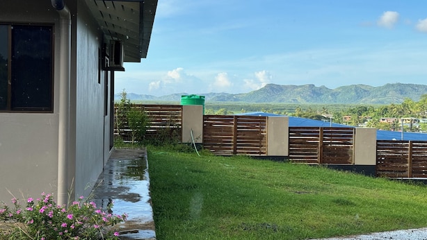 A modern building with a sloped roof, a grassy yard, and a view of distant mountains. - Dovu Residences (Labasa)