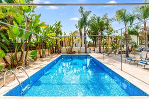 Une piscine rectangulaire à l’eau d’un bleu limpide, entourée d’une clôture métallique et agrémentée de diverses plantes tropicales.