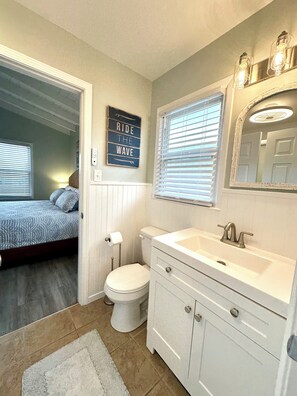 Une salle de bain avec des toilettes, un lavabo et un miroir. Il y a une affiche sur le mur avec l'inscription : « Profitez de l’instant présent ».