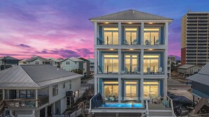 Un edificio de varios pisos frente a la playa, con una piscina en la planta baja, rodeado de otras construcciones residenciales.