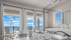 Habitación de hotel con un ventanal grande, una cama, una mesa de comedor con sillas y vista al océano.
