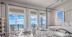 Ein Hotelzimmer mit Balkon, einem Essbereich mit Tisch für zwei Personen und einem Bett mit weißer Bettwäsche.