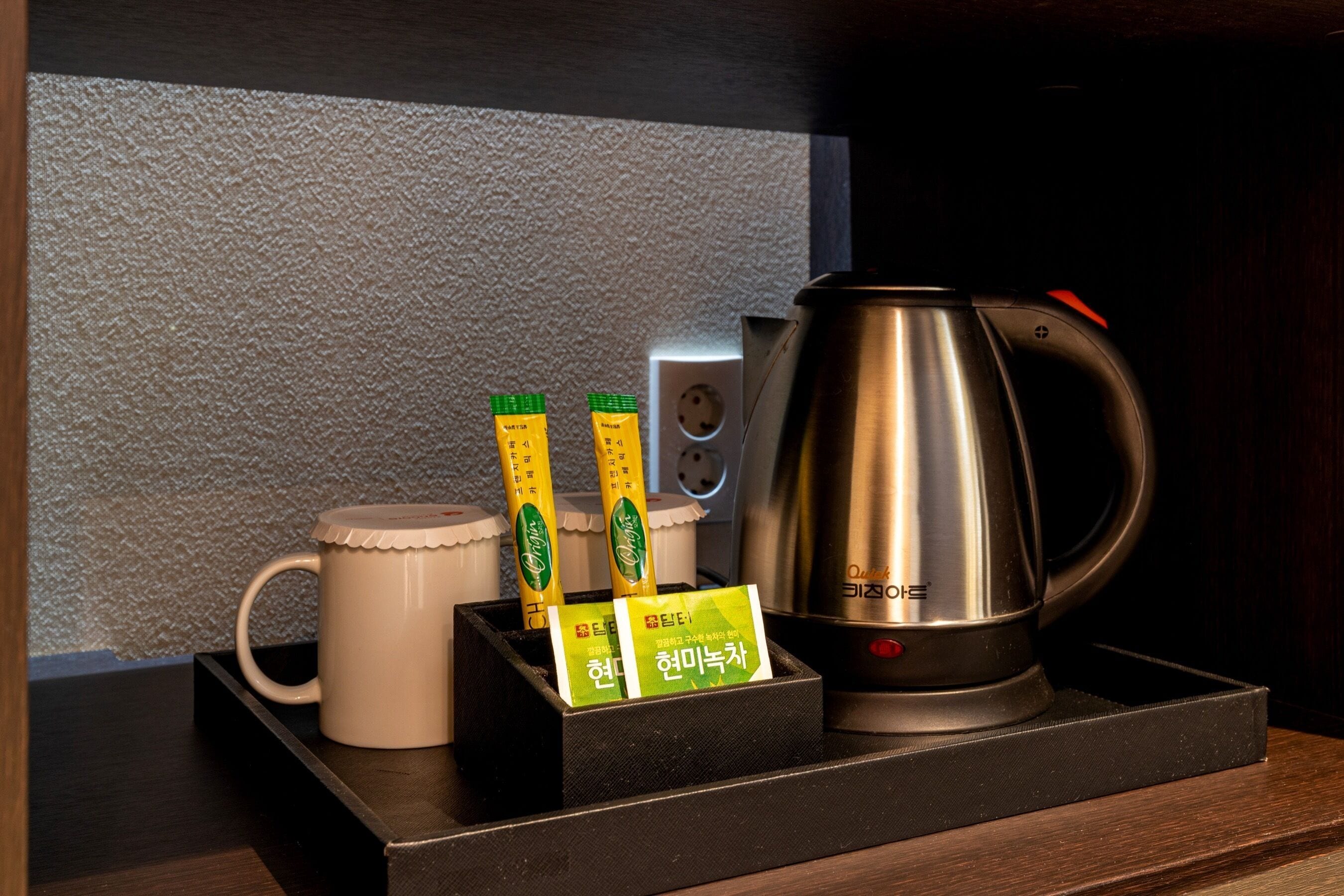 A coffee maker, a mug, and tea packets on a wooden tray.