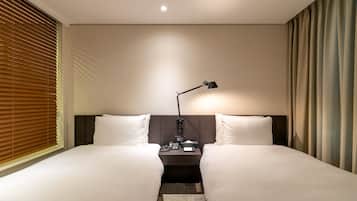 Habitación de hotel con dos camas, una mesita de noche, una lámpara y una ventana con persianas.